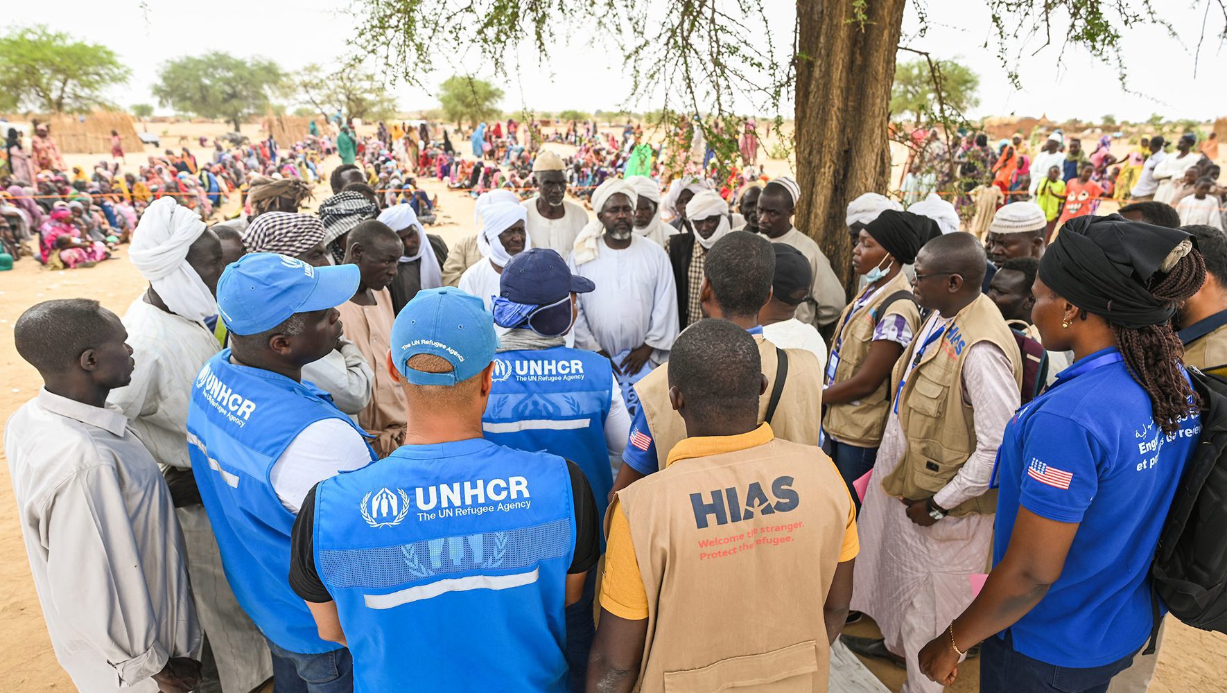 Aid workers talking to Sudanese refugee leaders outside under a tree